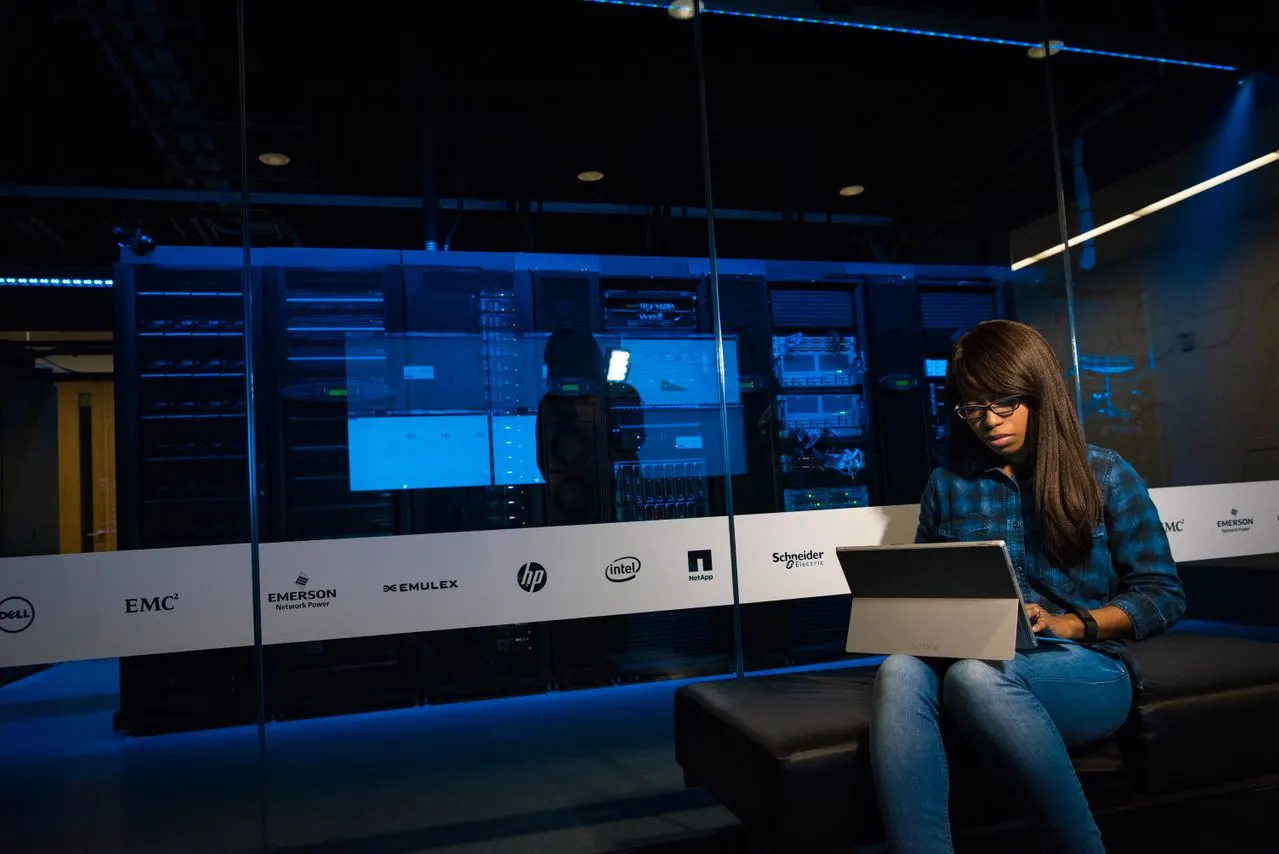 Une collaboratrice travaille sur une tablette devant une salle serveurs